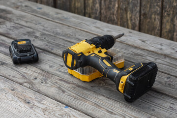 Yellow Cordless electric drill and battery charger on wooden background for DIY projects and...