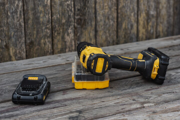 Yellow Cordless electric drill and battery charger on wooden background for DIY projects and...