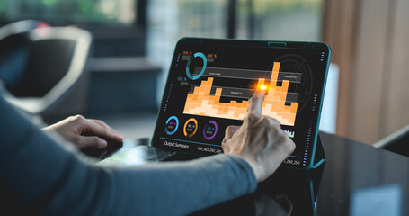 A person interacts with a digital tablet displaying graphical data in a modern setting.
