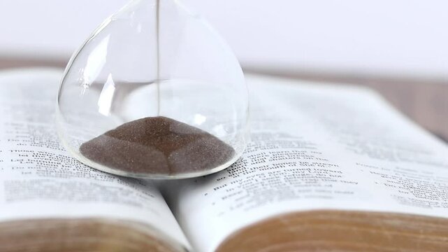 Sand falling in hourglass and open holy bible book. Close-up. Selective focus. Christian biblical concept of time and patience.