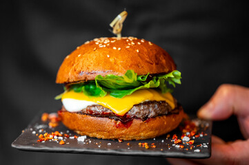 A close-up of a delicious cheeseburger with lettuce, cheese, and sauce, held on a black plate. The sesame seed bun adds an appealing touch to this mouthwatering dish.