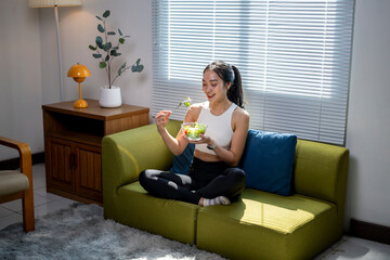 A woman is sitting on a couch eating a salad