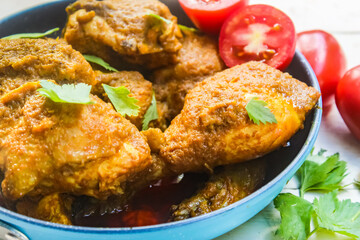 close up of chicken curry dish in a pan with tomatoes and celery on a wooden table