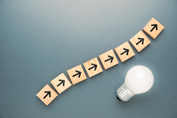 All wooden cubes with arrow symbol moving upward in the same direction, with glowing light bulb,...