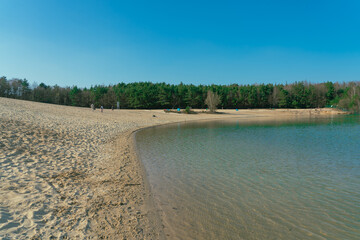 Shallow lake with sandy shore and forest in the background