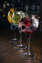 Assorted cocktails with orange, cucumber and berry garnishes served in balloon glasses on a rustic wood surface in a dimly lit bar, ideal for themes like bartending, drinks menu or nightlife.