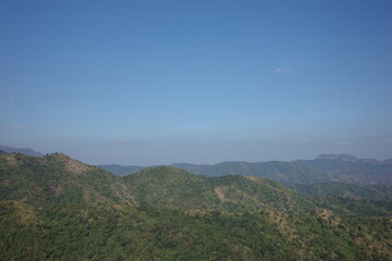Expansive mountain range covered in lush green forest under a clear blue sky. A tranquil, untouched natural landscape ideal for travel, conservation, hiking, and environmental themes.