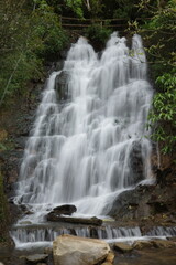 Fototapeta premium Beautiful waterfall cascading over dark rocks surrounded by lush green foliage in Sapa, Vietnam. The long exposure effect creates a silky water flow, capturing the serenity and power of nature.