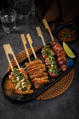 A black plate with four skewers of meat and a lime on it