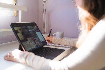 Female designer working from home reviewing website designs on a tablet and taking notes in a...
