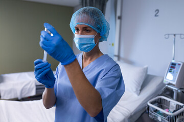 Mid-adult female nurse drawing medication vial into syringe in hospital room, with infusion pump