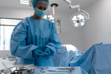 Female surgeon preparing instruments in operating room, using metal tray under surgical lights