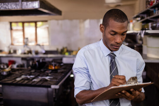 Mid-adult African American man using clipboard in commercial kitchen, with gas range, copy space