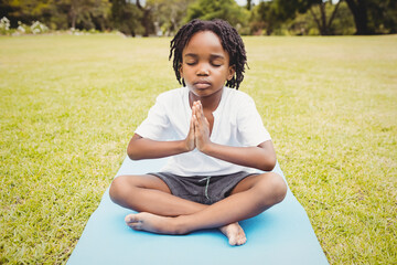 African American boy meditating on blue yoga mat in grassy field, enjoying calm and focus