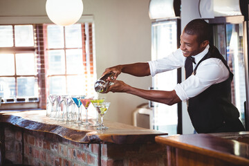 Mid-adult African American man pouring cocktail from shaker in indoor cocktail bar, copy space