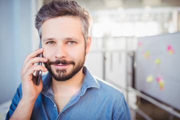 Mid adult man standing in office setting, holding smartphone to ear and making eye contact