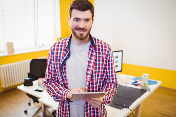 Male office worker holding tablet in modern office, with computer monitor, mouse pad and coffee cup