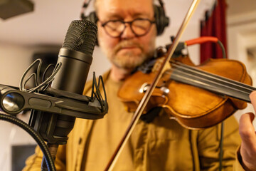 A man plays the violin in a recording studio, using a professional condenser microphone.