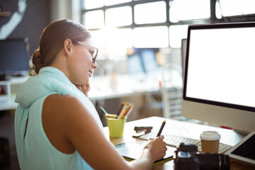 Woman leaning on hand using stylus on graphics tablet at office desk with camera, copy space
