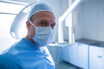 male surgeon standing in hospital operating room with overhead light and monitor, copy space
