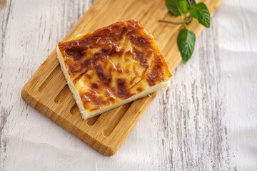 Slice of traditional Turkish Börek on wooden board. Food is served on a cutting board. The setup is minimalistic with a small green leafs. Selective focus.