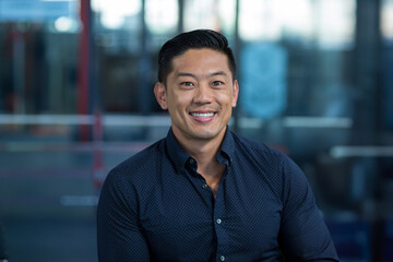 Fototapeta premium Asian man sitting in office lounge, smiling warmly at camera and projecting professional warmth
