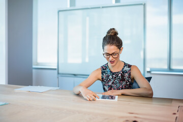 Young woman tapping on tablet in modern office meeting room, featuring wooden table and whiteboard