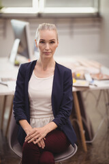 Mature woman sitting on gray molded chair in modern studio office, working with papers and monitor