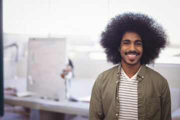 Indian man smiling at camera in office, with whiteboard scribbles scattered papers, copy space