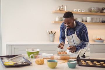 African American man cracking eggs in modern home kitchen, with egg carton and mixing bowls