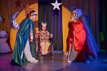 Full length shot from audience space of kids acting out knights battle on stage decorated with stars while playing in inclusive drama school for children