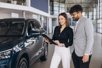 Saleswoman showing specifications of new car to customer at dealership