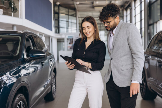 Saleswoman showing vehicle specifications to customer buying new car