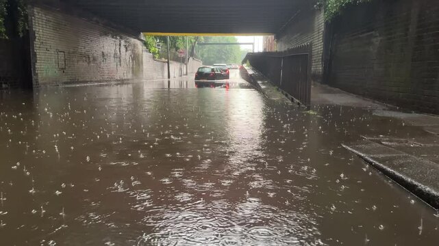 Two cars stranded under the bridge in torrential rain, yellow hazard lights flashing, road is closed.