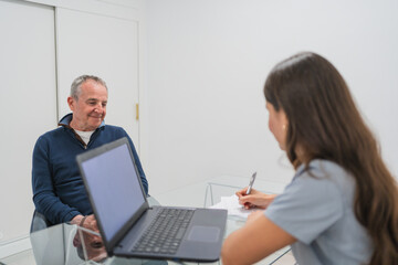 Obraz premium Physiotherapist taking notes during medical consultation with senior man in bright modern clinic