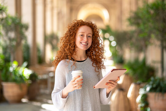 Smiling student holding coffee and tablet in university cloister