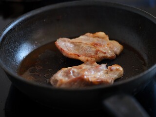 Two pork chops cooking in a frying pan