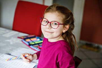 Little school girl learning at home. Elementary class student chid doing maths homework, writing...