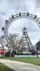Giant ferris wheel with red cabins towering above a park with bare trees and a cloudy sky. The image captures leisure, urban landmarks and seasonal atmosphere in a European amusement setting