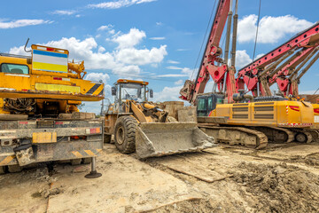 Heavy construction machinery including yellow loader and red drilling rig at outdoor site.