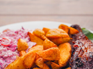 Simple meal with pork belly, potato wedges and pink coleslaw on white plate. Fine dinner with simple products.