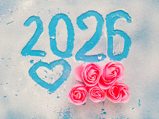 Glass with frost and hand written sign 2026 and heart and pink roses, . Blue background. New Year celebration concept.