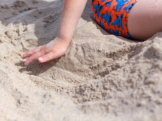 Child's hand playing with sea sand on the beach on a sunny day, texture, rest, vacation, free space for text.