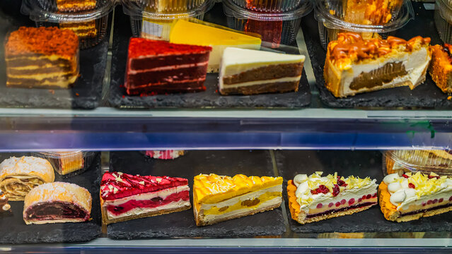 Assorted cakes and slices with colorful layers arranged in refrigerated display case. Dessert showcase reflects temptation, variety, gourmet appeal