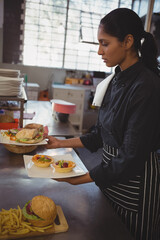 Indian woman chef plating tartlets and sandwiches on white plate in restaurant kitchen, copy space