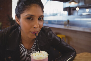 young Indian woman sipping pink milkshake at wooden café table, with whipped cream and black straw