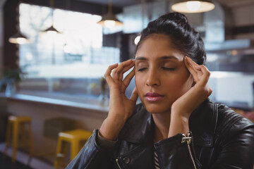 Indian woman sitting at table in modern cafe, pressing temples under industrial pendant lights