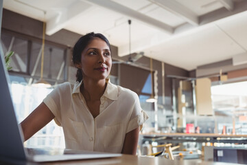Indian woman working on open laptop at wooden table in modern café, showing focus, copy space