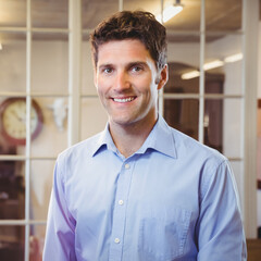 Man standing in office in front of white framed glass partition, with clock and bust sculpture