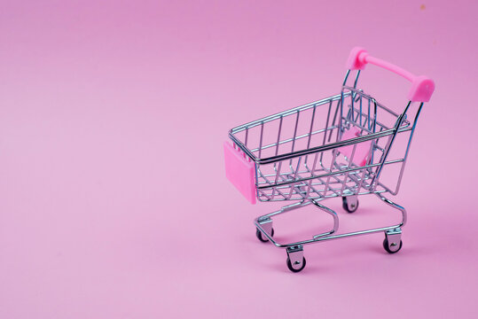 A mini shopping cart displayed prominently on a vibrant pink background for visual appeal and style